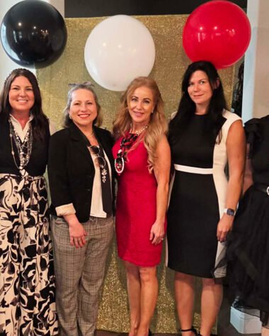 Corinna Slamons, co-hosts, and Women In Need representatives posing together at a “Devil Wears Prada” themed charity event in North Texas