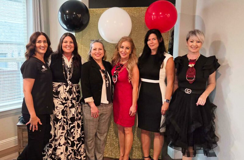 Corinna Slamons, co-hosts, and Women In Need representatives posing together at a “Devil Wears Prada” themed charity event in North Texas